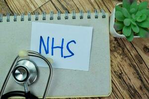 Concept of NHS write on sticky notes with stethoscope isolated on Wooden Table. photo