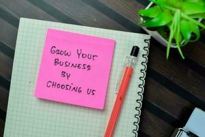 Concept of Grow Your Business by Choosing Us write on book isolated on Wooden Table. photo