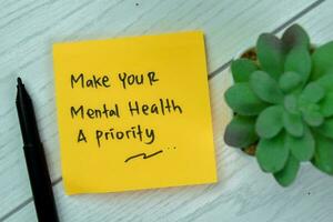 Concept of Make Your Mental Health A Priority write on sticky notes isolated on Wooden Table. photo