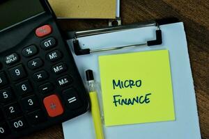 Concept of Micro Finance write on sticky notes with calculator isolated on Wooden Table. photo