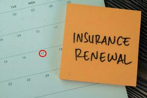 Concept of Insurance Renewal write on sticky notes with calendar isolated on Wooden Table. photo