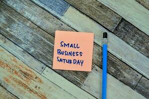 Concept of Small Business Saturday write on sticky notes isolated on Wooden Table. photo