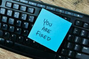 Concept of You Are Fired write on sticky notes isolated on Wooden Table. photo