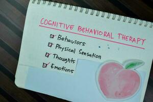 Concept of Cognitive Behavioral Therapy write on a book with keywords isolated on Wooden Table. photo