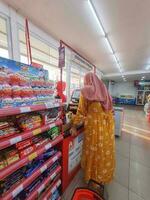 Jakarta, Indonesia in March 2023. A mother wearing a yellow negligee is paying at the Alfamart cashier. photo