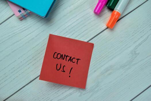 Concept of Contact Us write on sticky notes isolated on Wooden Table. photo