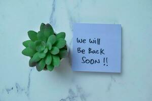 Concept of We Will Be Back Soon write on sticky notes isolated on Wooden Table. photo