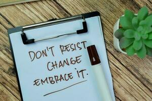 Concept of Don't Resist Change Embrace It write on paperwork isolated on Wooden Table. photo