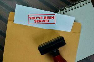 Concept of Red Handle Rubber Stamper and You've been Served text above from brown envelope isolated on on Wooden Table. photo