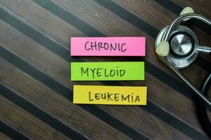 Concept of Chronic Myeloid Leukemia write on sticky notes with stethoscope isolated on Wooden Table. photo