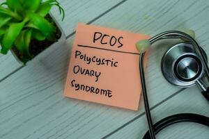 Concept of POCS Polycystic Ovary Syndrome write on sticky notes with stethoscope isolated on Wooden Table. photo