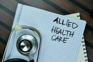 Concept of Allied Health Care write on book with stethoscope isolated on Wooden Table. photo