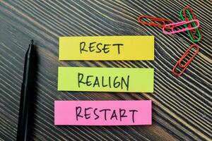 Concept of Reset, Realign, Restart write on sticky notes isolated on Wooden Table. photo