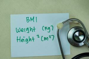 Concept of BMI - Weight and Height write on sticky notes with stethoscope isolated on Wooden Table. photo