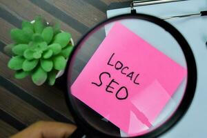 Concept of Local SEO write on sticky notes with magnifying glass isolated on Wooden Table. photo