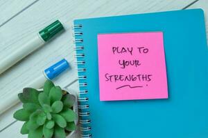 Concept of Play To Your Strengths write on sticky notes isolated on Wooden Table. photo