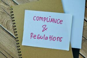 Concept of Compliance and Regulations write on sticky notes isolated on Wooden Table. photo