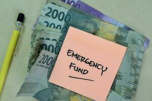 Concept of Emergency Fund write on sticky notes with Indonesian Currency isolated on Wooden Table. photo