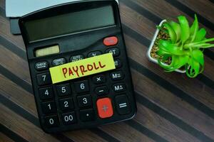 Concept of Payroll write on sticky notes with calculator isolated on Wooden Table. photo