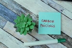 Concept of Carbon Pricings write on sticky notes isolated on Wooden Table. photo