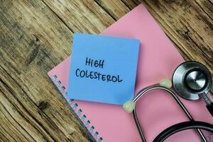 Concept of High Colesterol write on sticky notes with stethoscope isolated on Wooden Table. photo