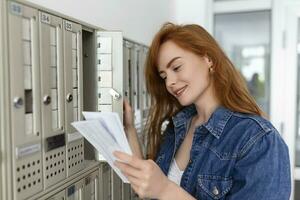 Positive casually dressed woman holding new letter from postal delivery, getting her post out of her letterbox photo