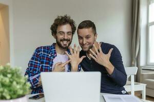 Gay lovers video calling their friends announcing engagement . Two young gay lovers smiling cheerfully while taking online after getting engaged. Happy gay man showing off his ring with his partner. photo