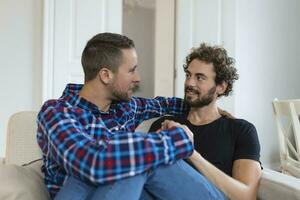 alegre joven gay Pareja sentado juntos. dos cariñoso masculino amantes sonriente alegremente mientras abrazando cada otro. joven gay cupé siendo romántico. foto