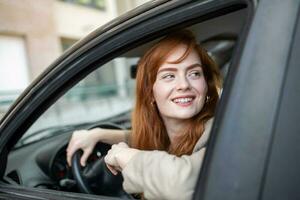 Joyful redhead woman inside of car looking back from driver seat while driving during the day. photo