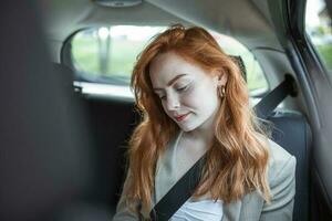 Beautiful young businesswoman sitting on back seat of a car and looking at mobile phone. Female business executive travelling by a cab. photo