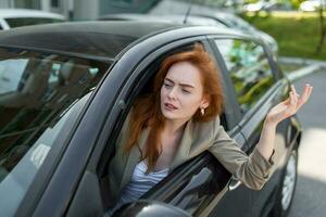 displeased woman looking out from side window and pointing with hand while driving car on blurred foreground photo