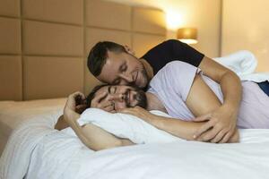 Gay couple embracing each other with their eyes closed. Two young male lovers touching their faces together while lying in bed in the morning. Affectionate young gay couple bonding at home. photo