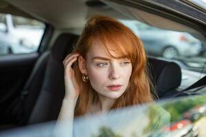 Beautiful young businesswoman sitting on back seat of a car and looking outside the window. Female business executive travelling by a cab. photo