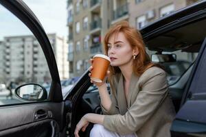 Happy young woman with coffee having a brake in her car. Side view of woman with coffee to go in hand. Young woman drinking coffee in her car photo