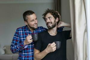 joven gay Pareja en amor mirando fuera el ventana. dos joven andrógino hombres sonriente juntos y teniendo café. foto