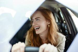 Beautiful smiling young redhead woman behind steering wheel driving car. photo