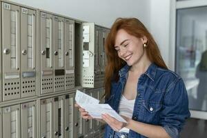 Positive casually dressed woman holding new letter from postal delivery, getting her post out of her letterbox photo