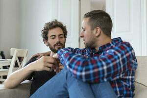 Cheerful young gay couple sitting together. Two affectionate male lovers smiling cheerfully while embracing each other. Young gay coupe being romantic. photo