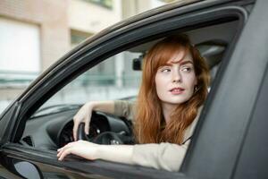Joyful redhead woman inside of car looking back from driver seat while driving during the day. photo
