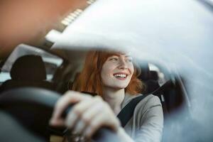 Beautiful smiling young redhead woman behind steering wheel driving car. photo