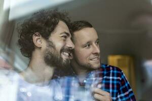 joven gay Pareja en amor mirando fuera el ventana. dos joven andrógino hombres sonriente juntos y teniendo café. foto