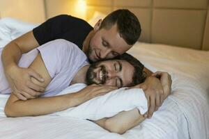 Gay couple embracing each other with their eyes closed. Two young male lovers touching their faces together while lying in bed in the morning. Affectionate young gay couple bonding at home. photo