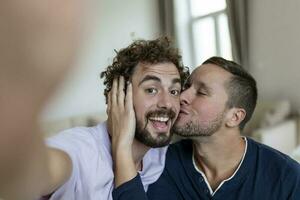 hermoso gay hombre sentado juntos a hogar tomando selfie con móvil teléfono. gay hombre con su compañero sentado por tomando un yo retrato utilizando inteligente teléfono. foto