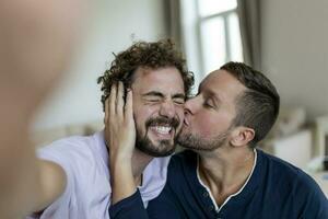 hermoso gay hombre sentado juntos a hogar tomando selfie con móvil teléfono. gay hombre con su compañero sentado por tomando un yo retrato utilizando inteligente teléfono. foto