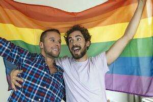 dos joven gay amantes mirando a cada otro afectuosamente. dos joven masculino amantes en pie juntos en contra un orgullo bandera. cariñoso joven gay Pareja compartiendo un romántico momento juntos. foto