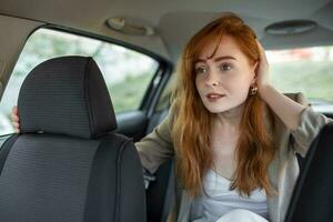 scared woman holding hand on head while riding in car on blurred foreground photo