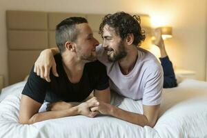 contento gay Pareja acostado abajo en el cama a hogar, abrazando y galanteo. lgbt gay Pareja amor momentos felicidad concepto foto