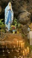 Statue of Holy Virgin Mary in Roman Catholic Church, in the cave of virgin mary, in a rock cave chapel Catholic Church with tropical flowers around photo