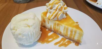 un rebanada de caramelo queso pastel con caramelo jarabe en parte superior y azotado crema y vainilla hielo crema servido en blanco plato foto