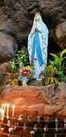 Statue of Holy Virgin Mary in Roman Catholic Church, in the cave of virgin mary, in a rock cave chapel Catholic Church with tropical flowers around photo